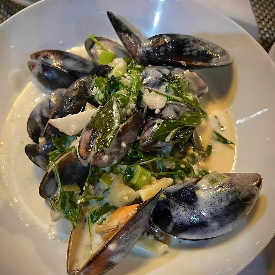 Randy's Bistro's mussels in a creamy sauce with green herbs and vegetables, served in a white bowl.