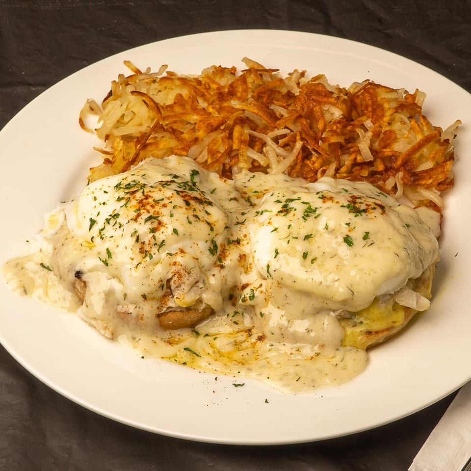 Randy's Bistro's Eggs Benedict with creamy sauce, herbs, and a side of crispy hash browns.