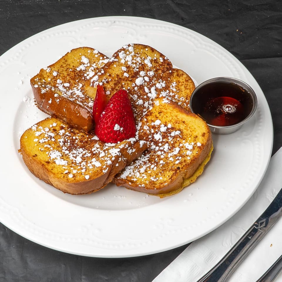Randy's Bistro French toast, powdered sugar, strawberries, and syrup on a white plate.